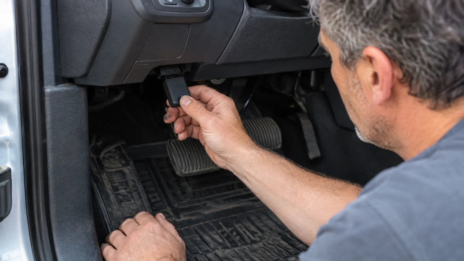a mechanic's hand plugging the Bluetooth scanner into the diagnostic port under a truck dashboard
